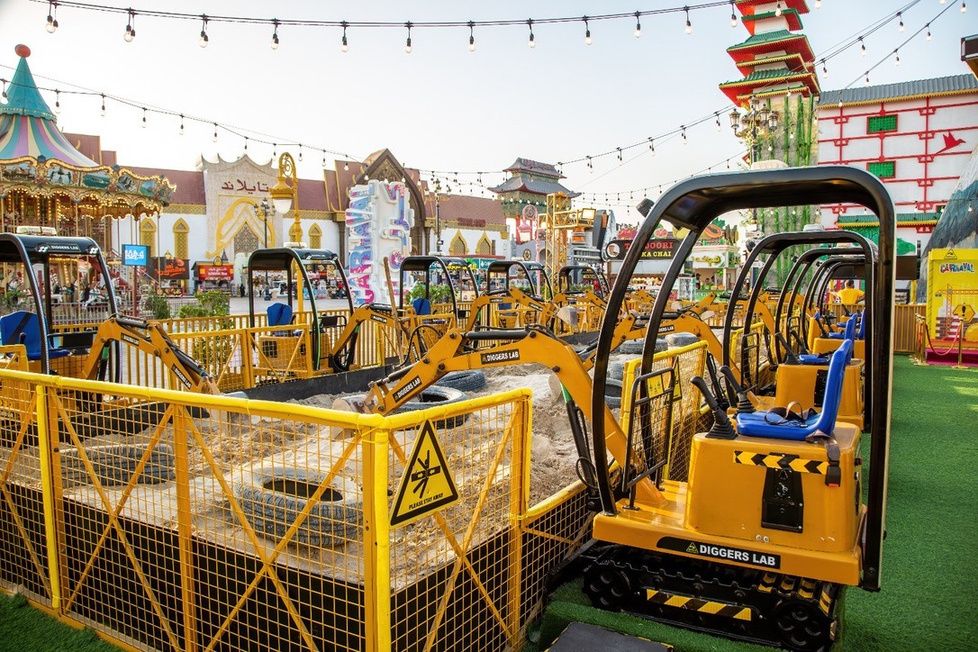 Mini excavator ride-ons in a fenced sand pit at an outdoor destination